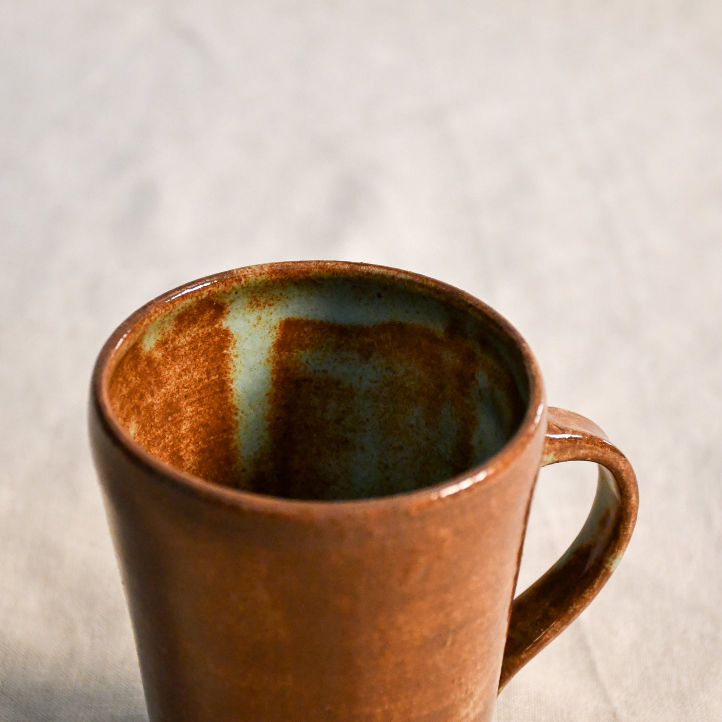 Close-up of a handmade ceramic mug showcasing the Heirloom Blue glaze interior with soft blue-green variation and rich rust undertones.