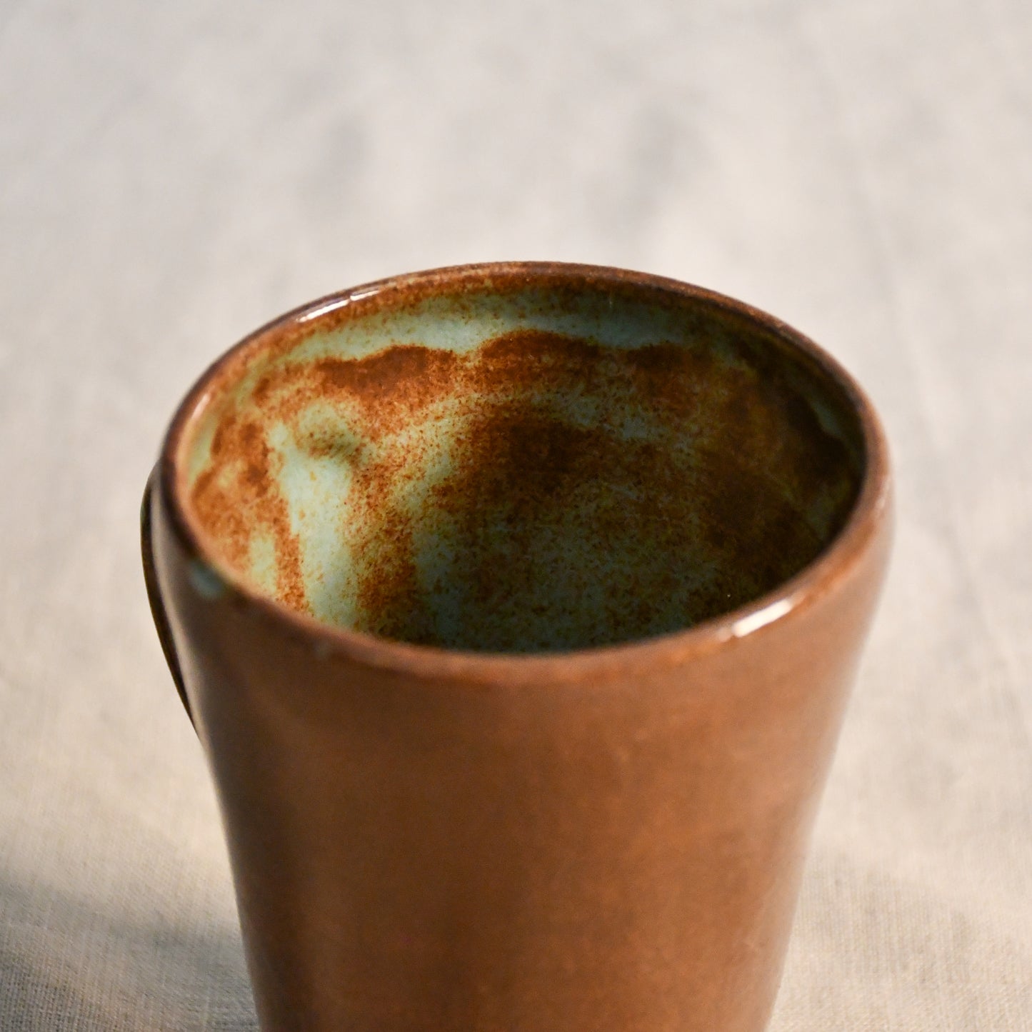 Detailed view of the Heirloom Blue glaze inside a wheel-thrown pottery mug, highlighting organic blue-green pooling and earthy brown speckling.