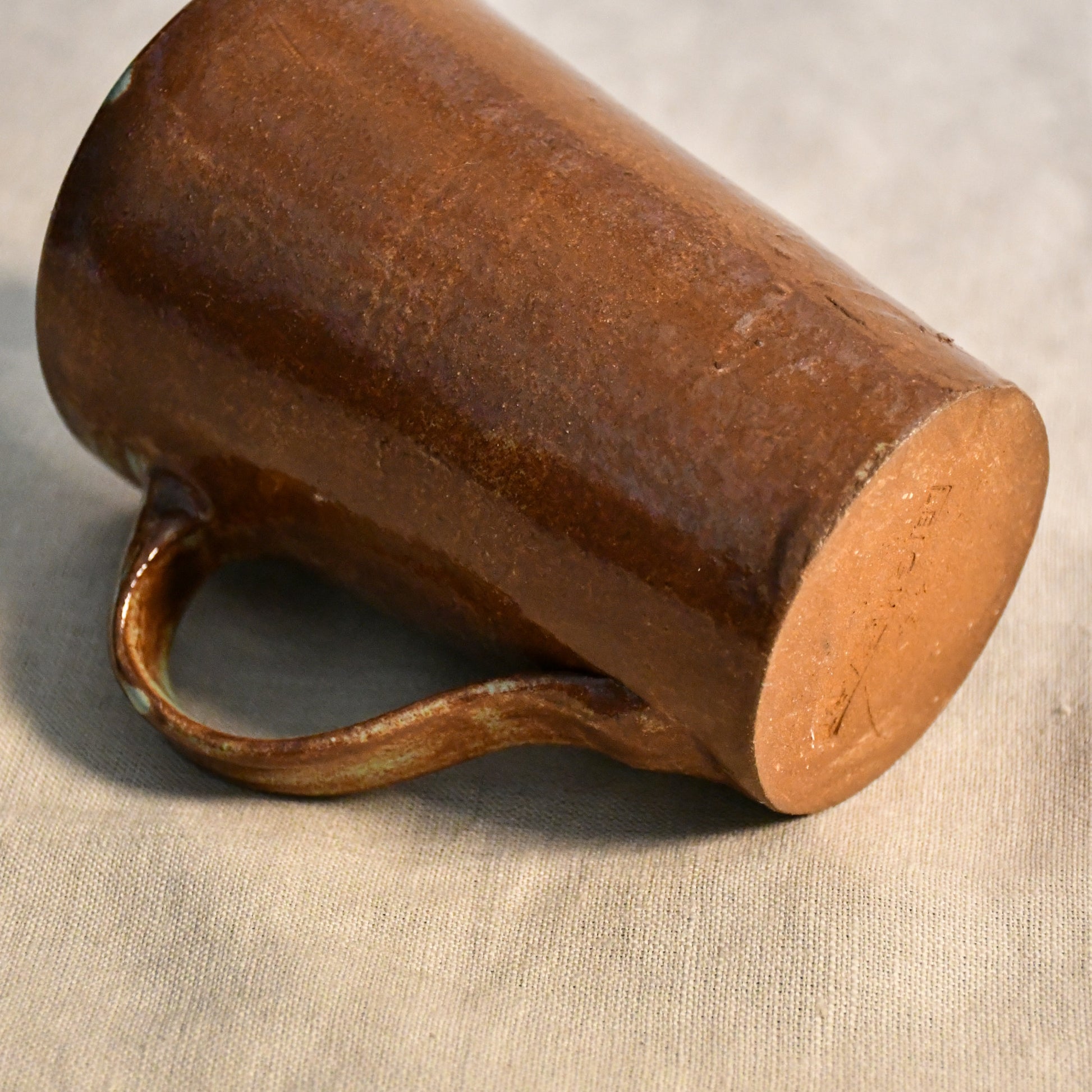 Underside of a handmade stoneware mug showing the unglazed foot and signed base beneath a Heirloom Blue glazed exterior.