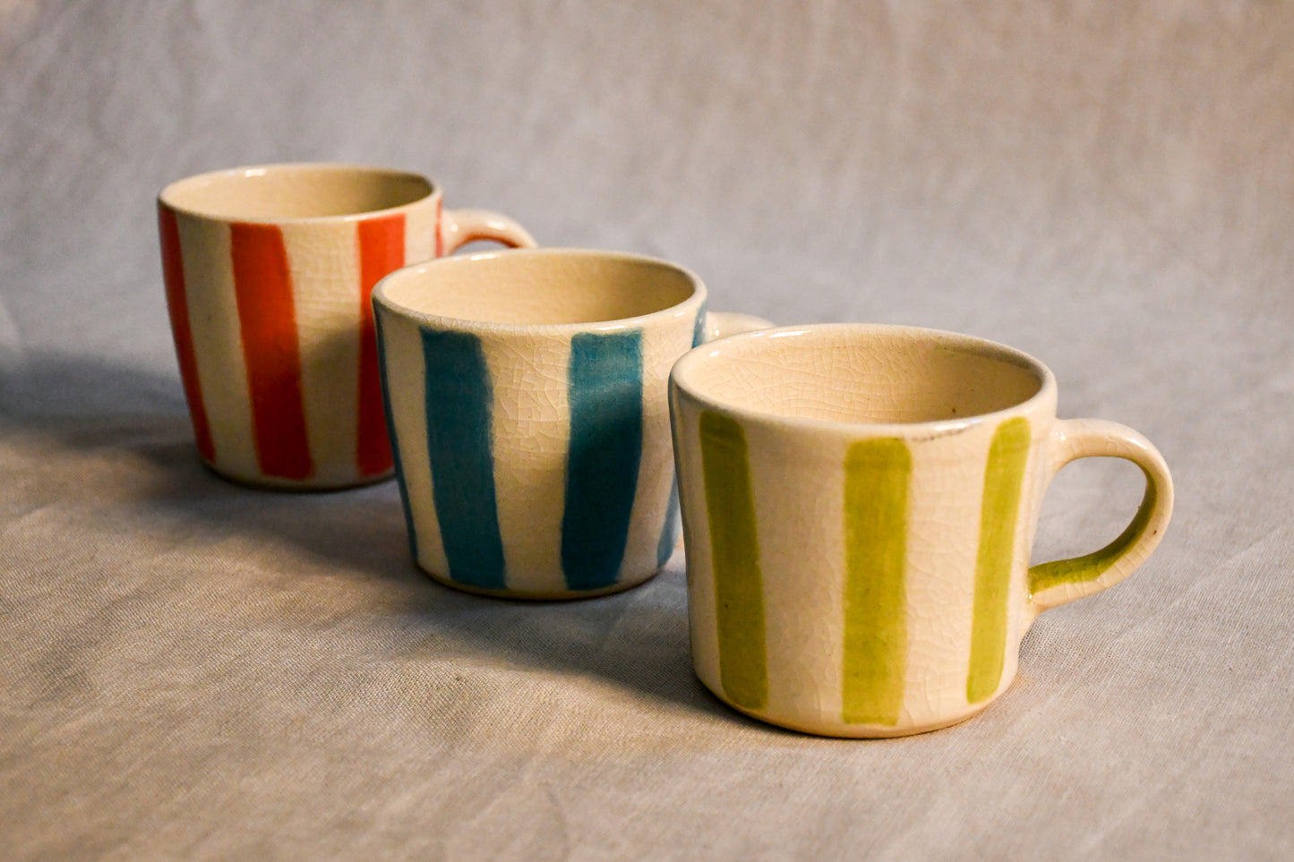 The Striped Trio mini espresso mugs featuring hand-painted turquoise, lime, and coral stripes on creamy stoneware with a crackled clear glaze finish from the Clayground collection.