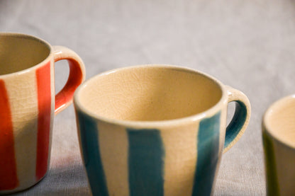 Close-up of a handmade turquoise striped mini mug with a creamy interior and delicate crazing beneath a clear glaze.