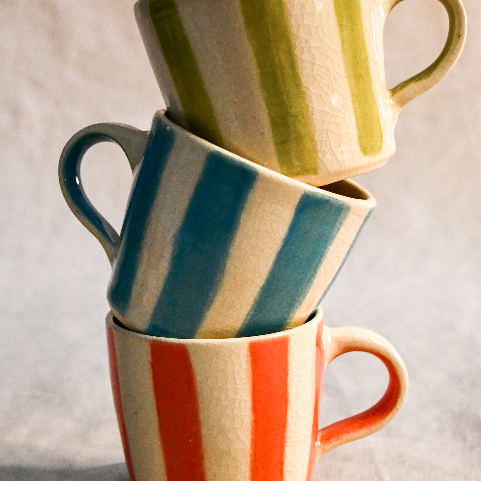 Stacked set of three handmade mini espresso mugs with turquoise, lime, and coral stripes finished in a crackled clear glaze.