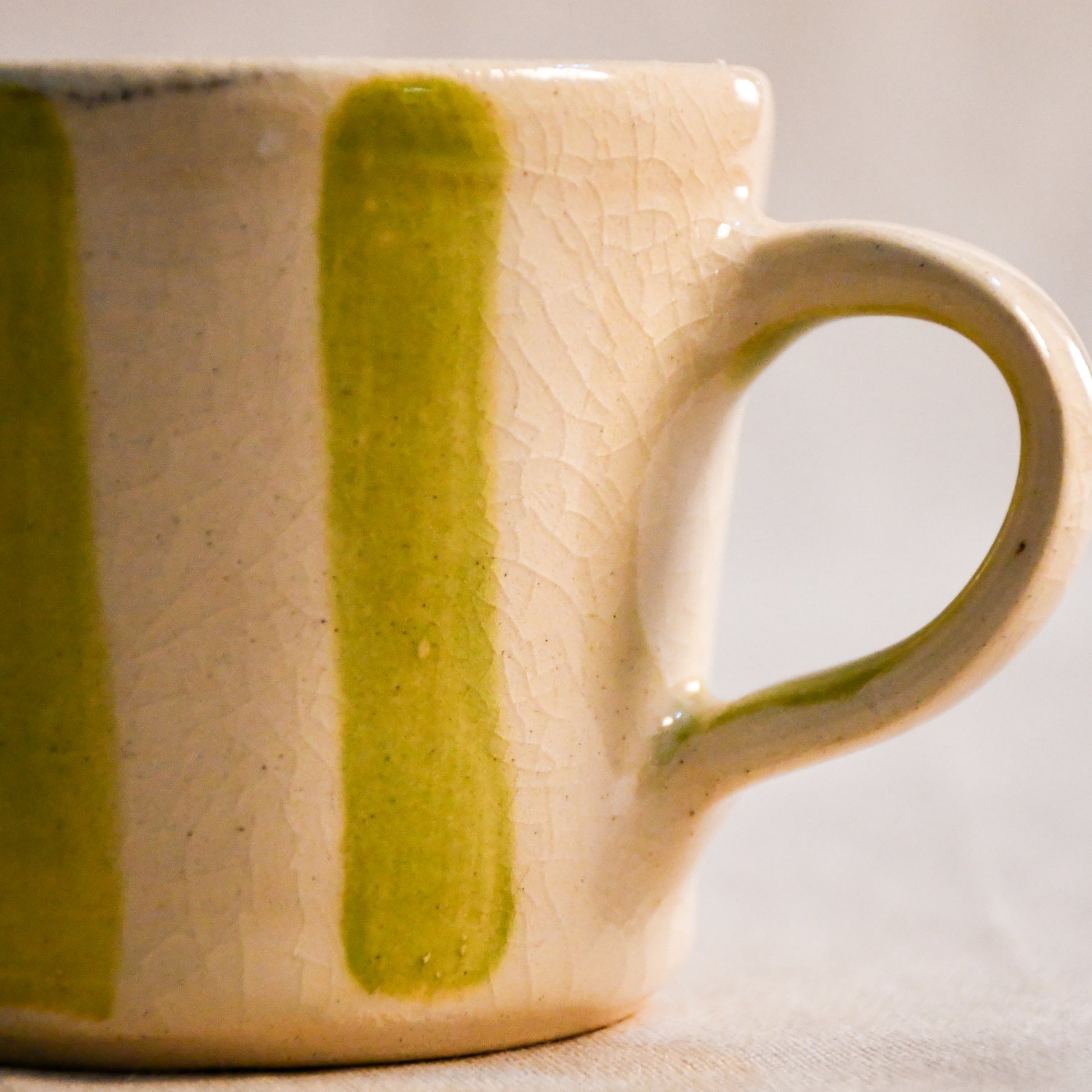 Detail of a lime striped espresso mug featuring a handmade handle and naturally crazed clear glaze over creamy stoneware.
