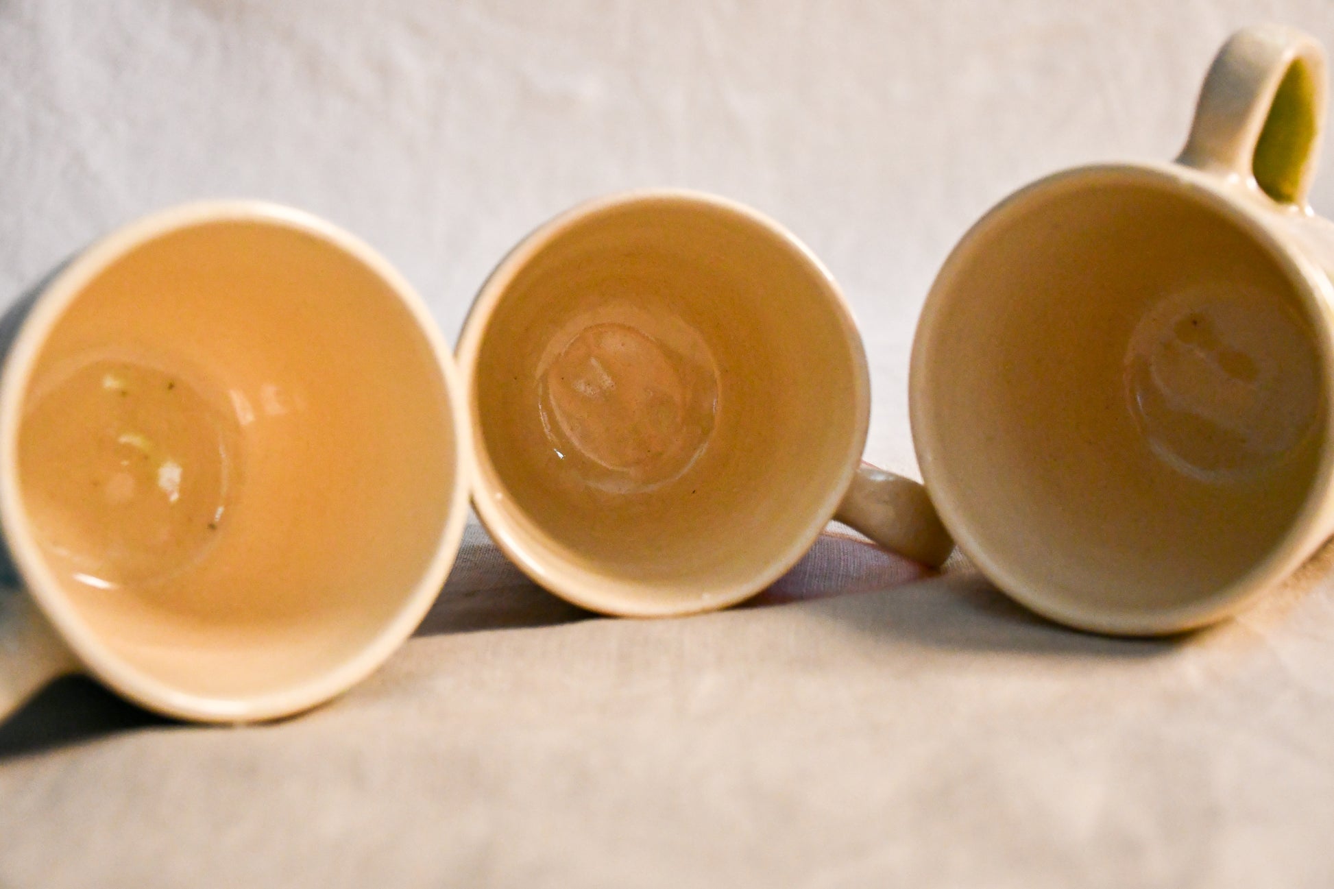 View of three handmade mini espresso mugs revealing their creamy glazed interiors and petite size.