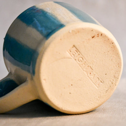 Underside of the turquoise striped mini mug showing the Leigh Art maker's mark and unglazed stoneware foot.